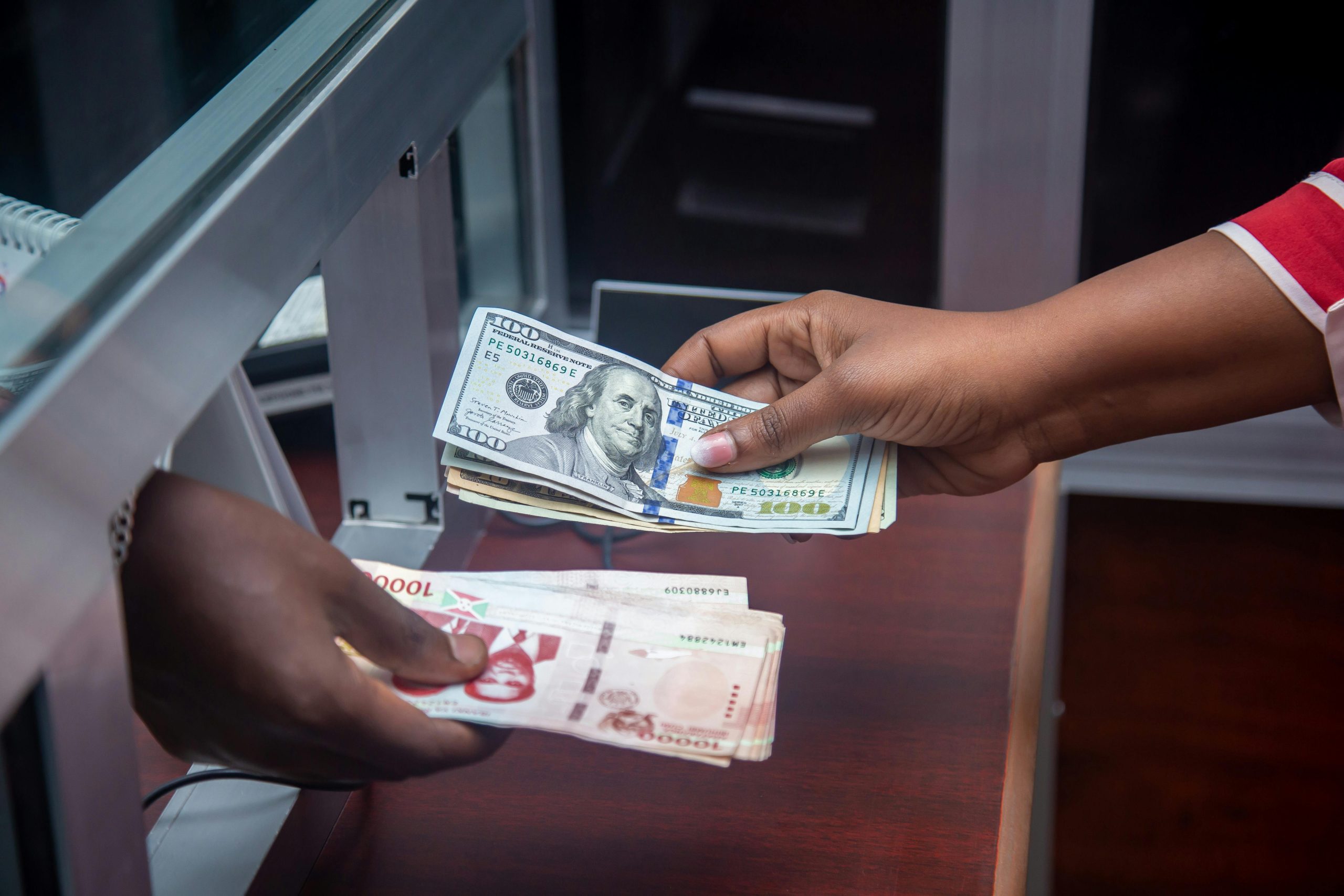 Hands exchanging US and local currency at a bank counter, signifying international finance.